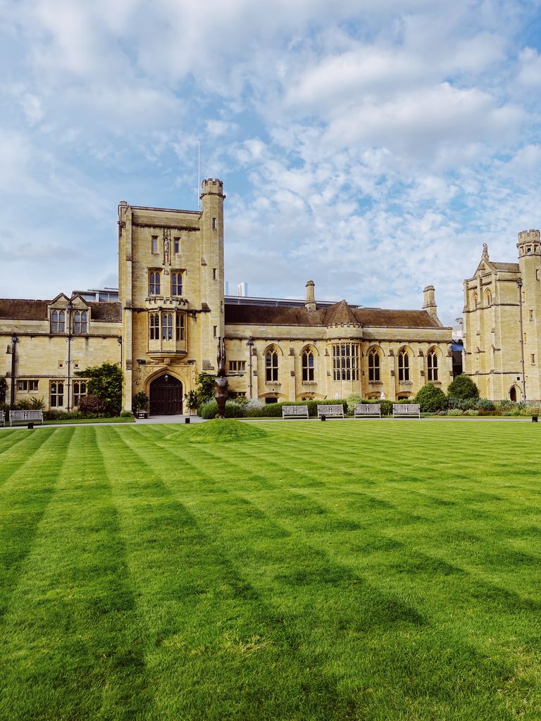A historic university building with an expansive green lawn under a blue sky.