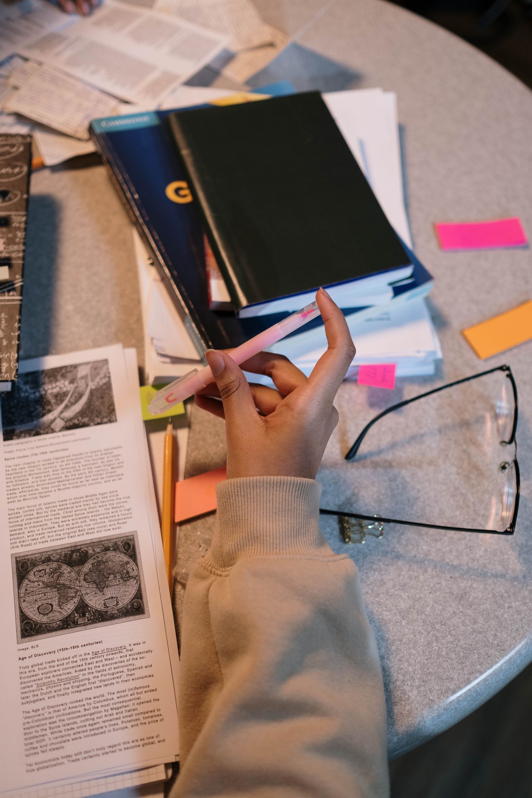 A student holding a pen surrounded by books and notes, focusing on study material.