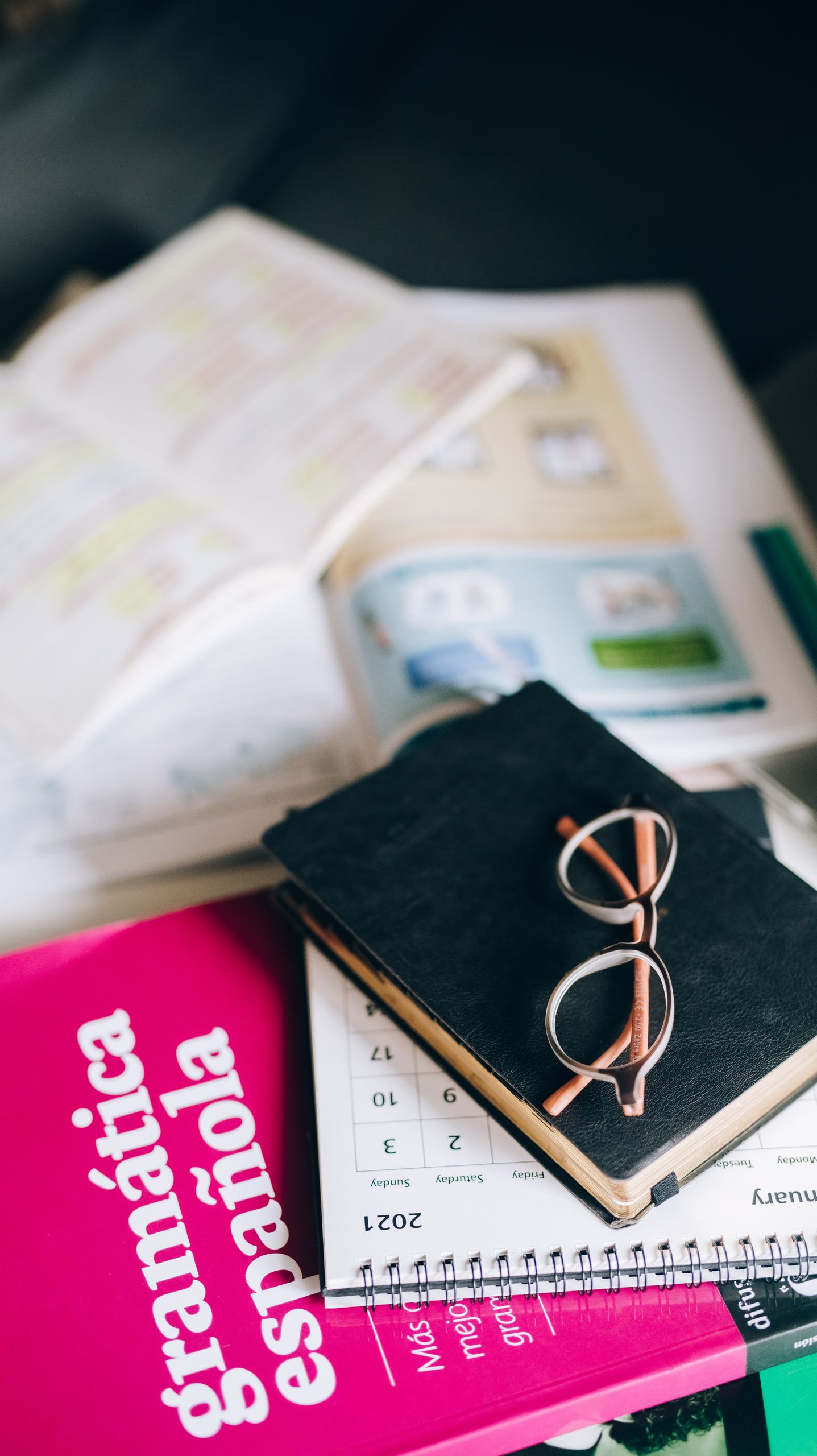 A study setup with a Spanish grammar book, calendar, and eyeglasses on a desk, suggesting focused learning.