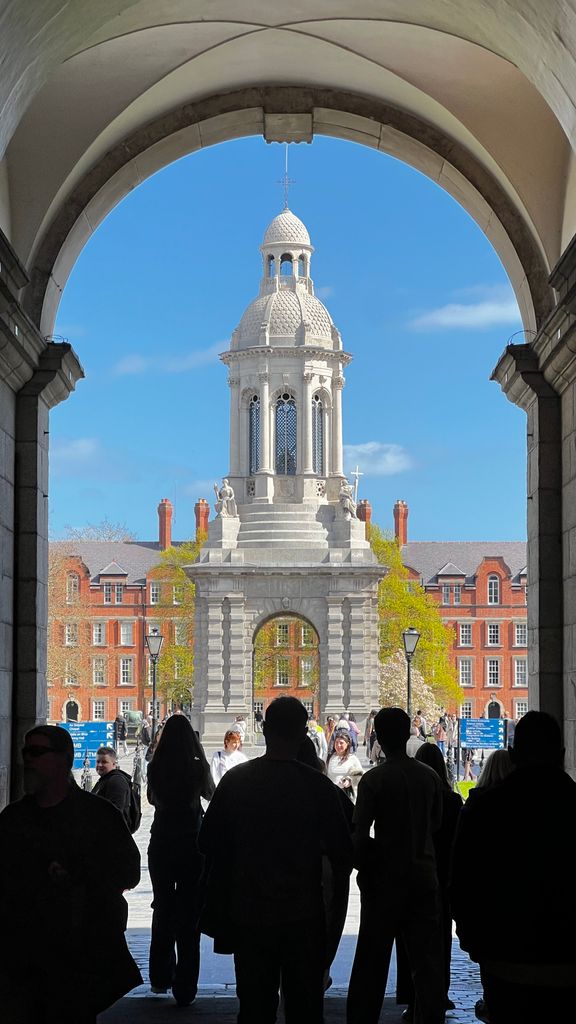View of the iconic Campanile in Trinity College, Dublin, framed by an archway on a sunny day.